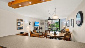 A modern kitchen with a granite countertop, wooden chairs, a dining table, and a ceiling fan. - Kamaole Sands 7-109 - Romantic Getaway, Beautiful Renovation, Large Lanai, & AC! (Kihei)
