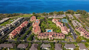 An aerial view of a resort with multiple buildings, a swimming pool, and a view of the ocean.