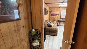 A wooden interior with a checkered sofa, a small table with decorative items, and a door leading to another room.