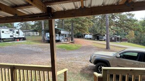 A covered outdoor area with a wooden deck, a metal roof, and a view of a campground with RVs and a car.