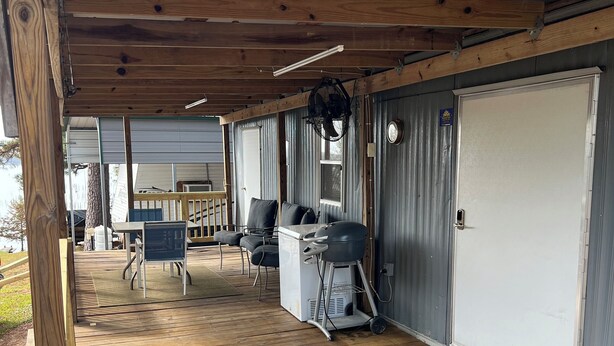 A covered deck with outdoor seating, a grill, and a door with a welcome mat.