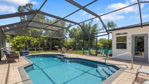 A covered swimming pool with a glass enclosure, surrounded by lounge chairs and a patio area.