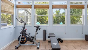 A home gym with exercise equipment, large windows, and a view of greenery.