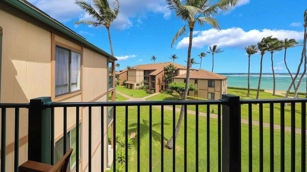 A residential area with a view of the ocean, palm trees, and a building with a balcony.