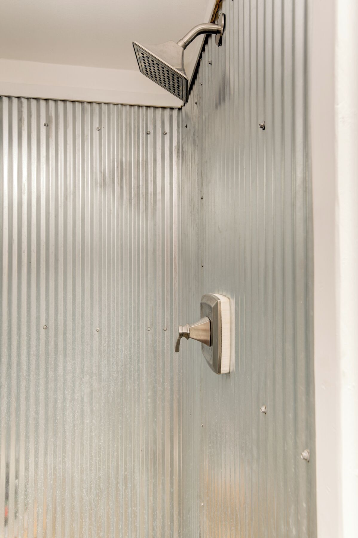 A shower with a handheld showerhead mounted on a corrugated metal wall.
