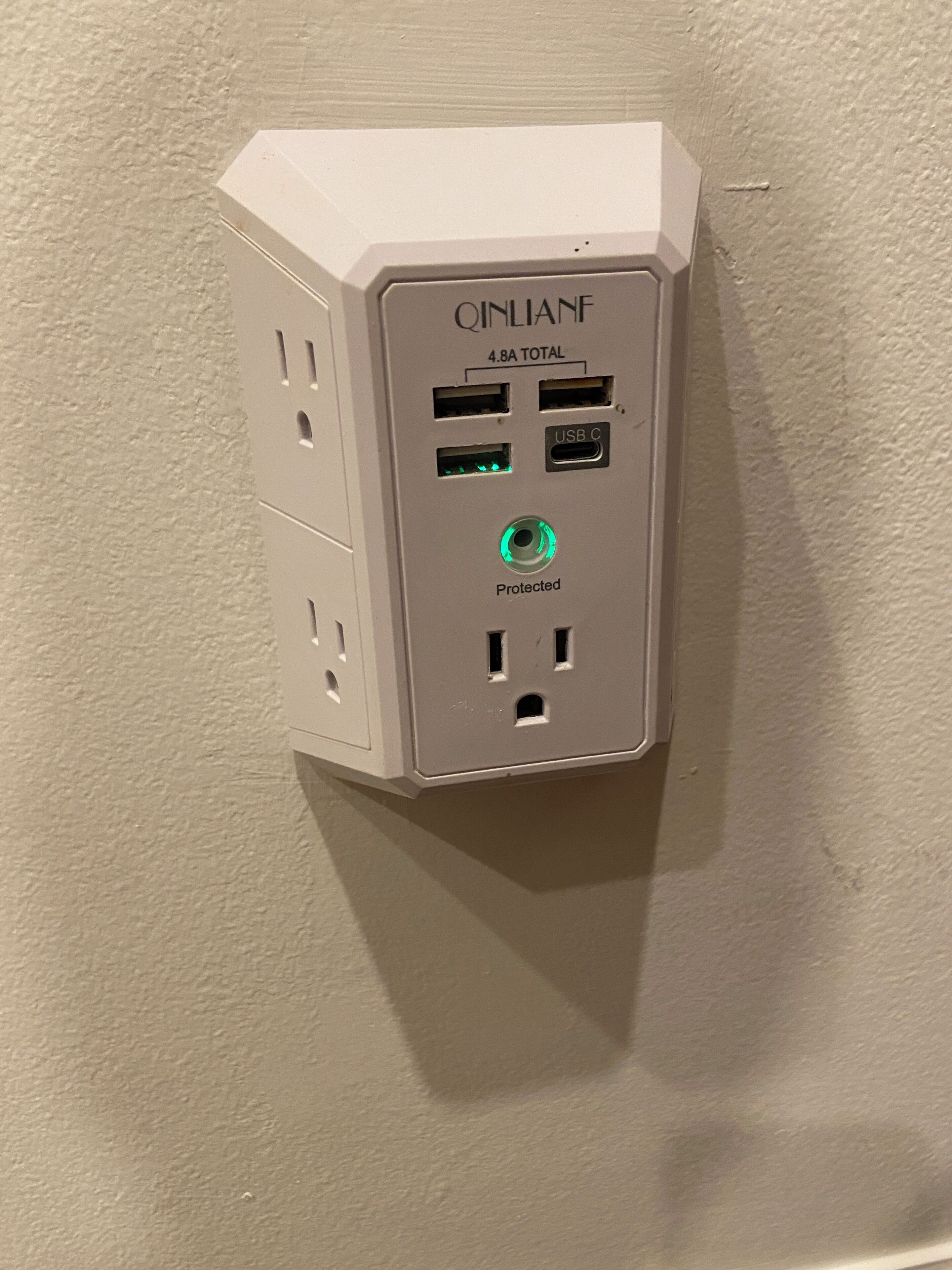 A white electrical outlet box with multiple USB ports, labeled "QINLANE 4.8A TOTAL," and a green indicator light.
