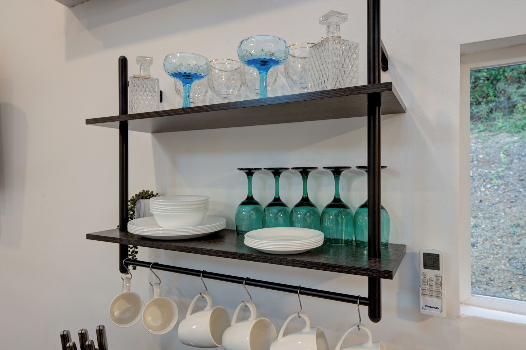 A kitchen shelf with glassware, plates, and cups.