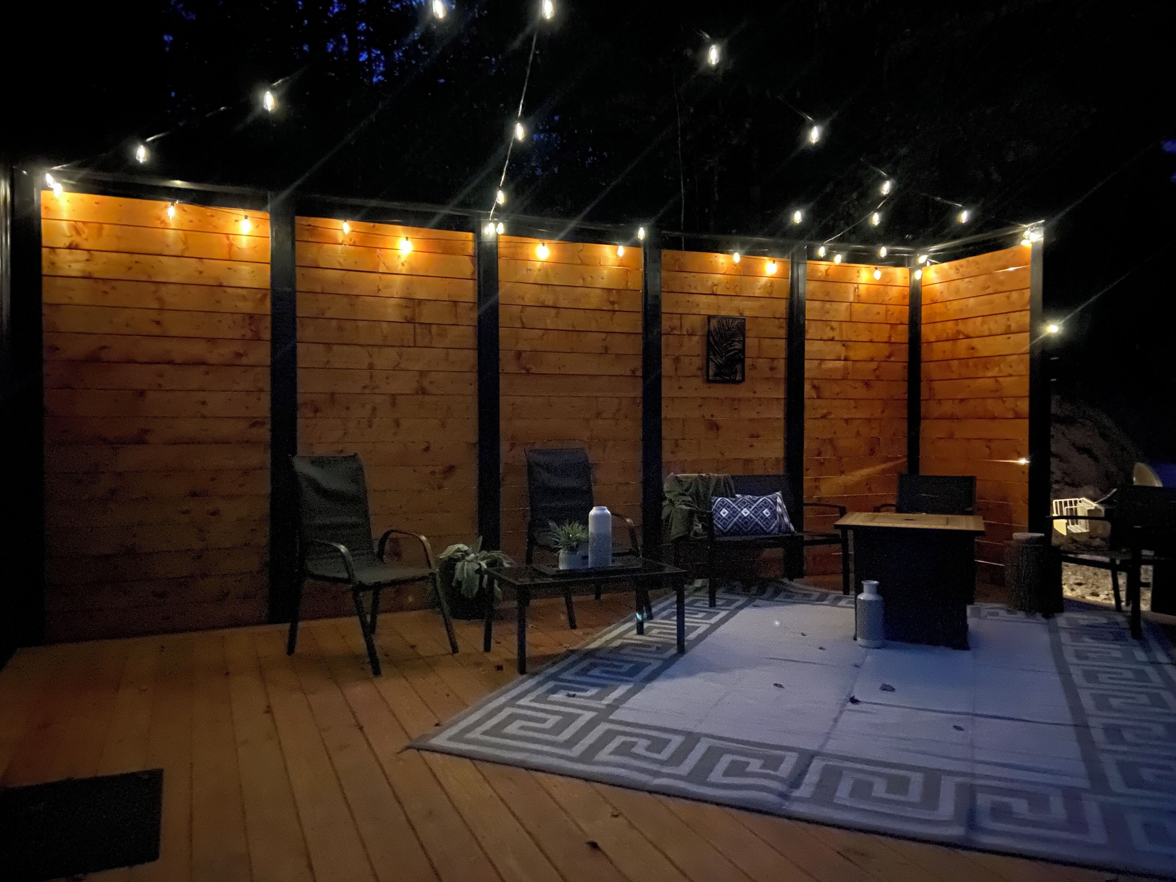 An outdoor patio area with wooden walls, string lights, and seating.