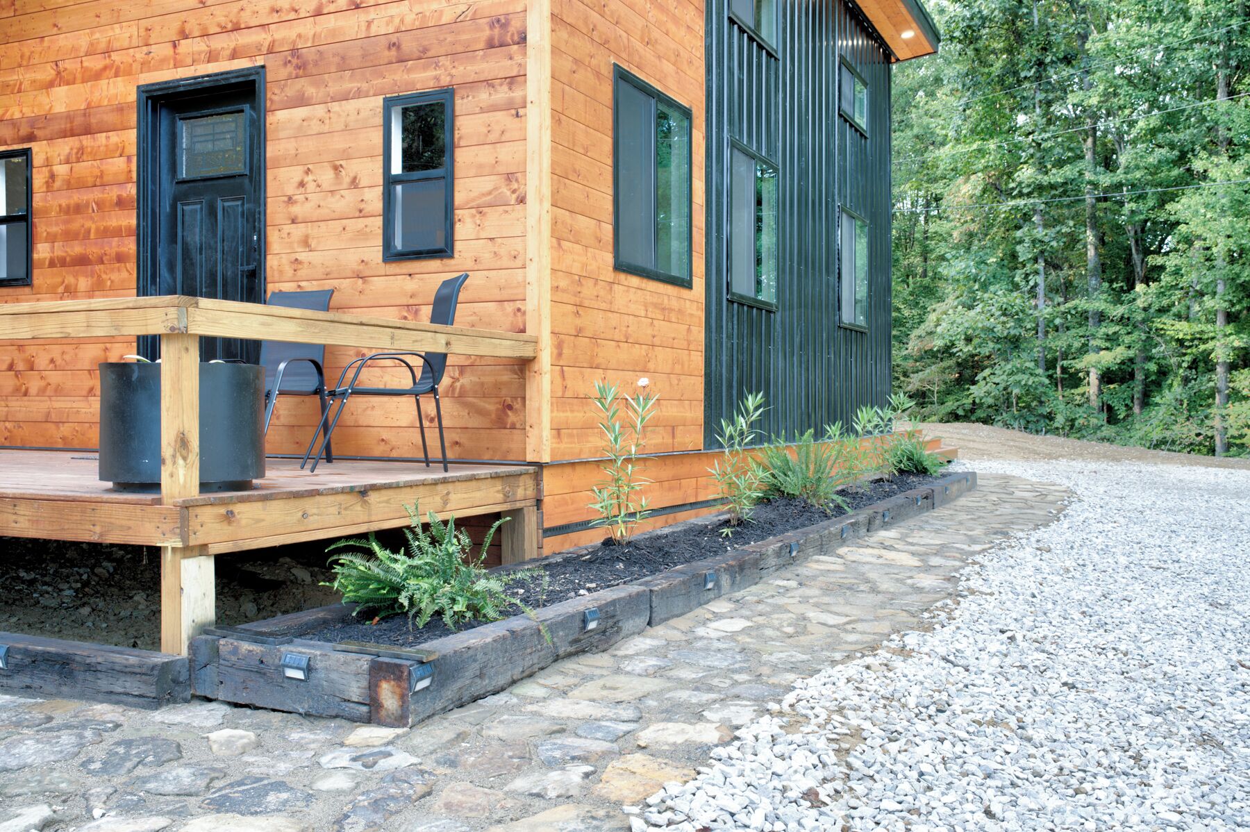 A wooden cabin with a deck, two black doors, and a window.