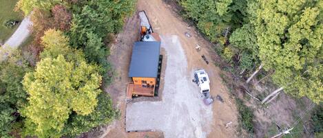 An aerial view of a cabin with a gravel driveway, surrounded by dense forest.