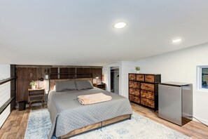 A modern bedroom with a large bed, a wooden wardrobe, a built-in desk, and a refrigerator.