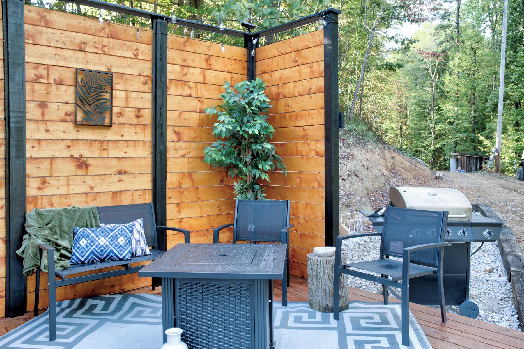 A wooden deck with a table and chairs, a grill, and a potted plant.