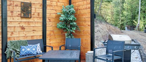 A wooden deck with a table and chairs, a grill, and a potted plant.