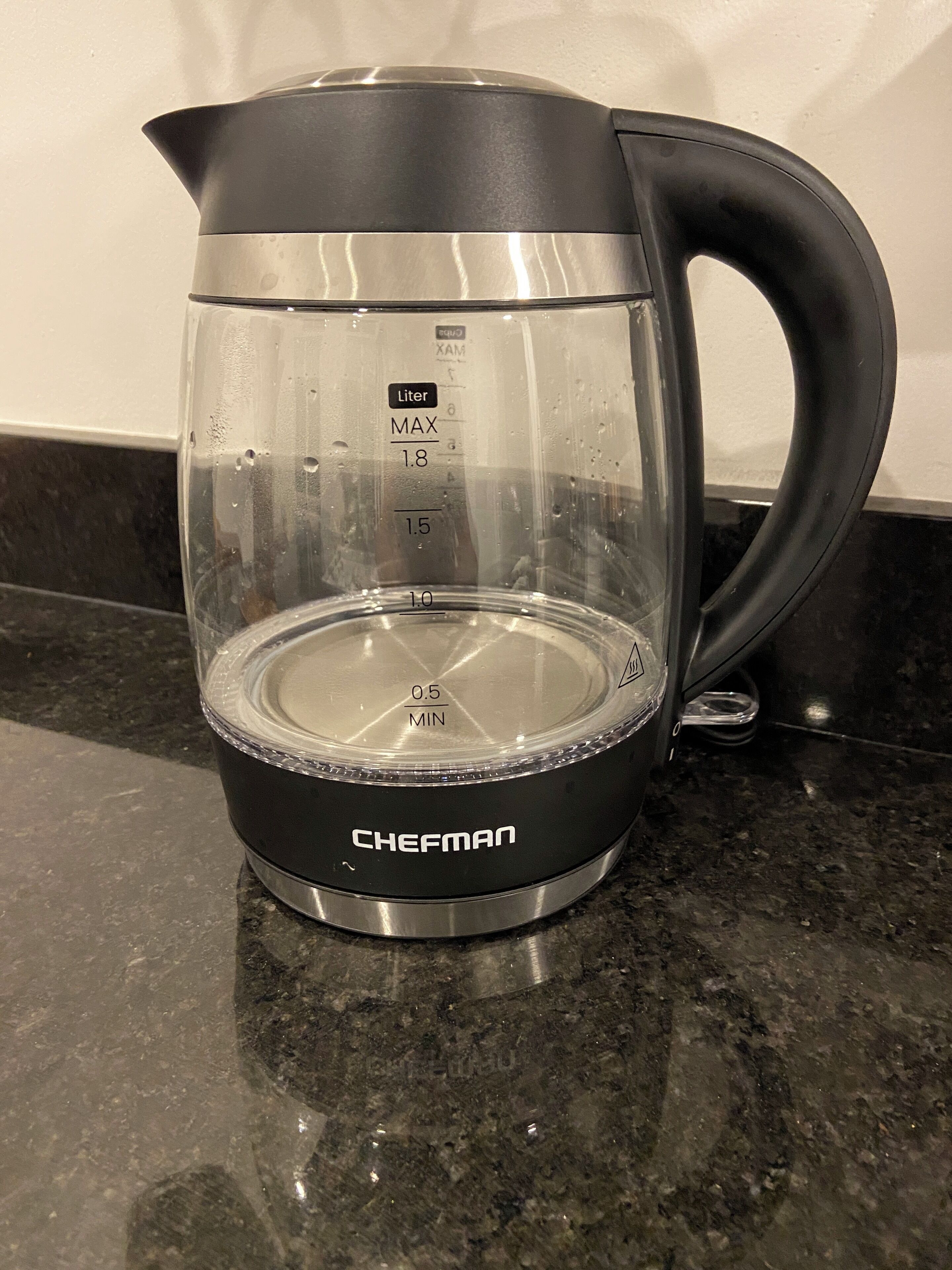 A black and transparent electric kettle with measurement markings on the side, placed on a granite countertop.