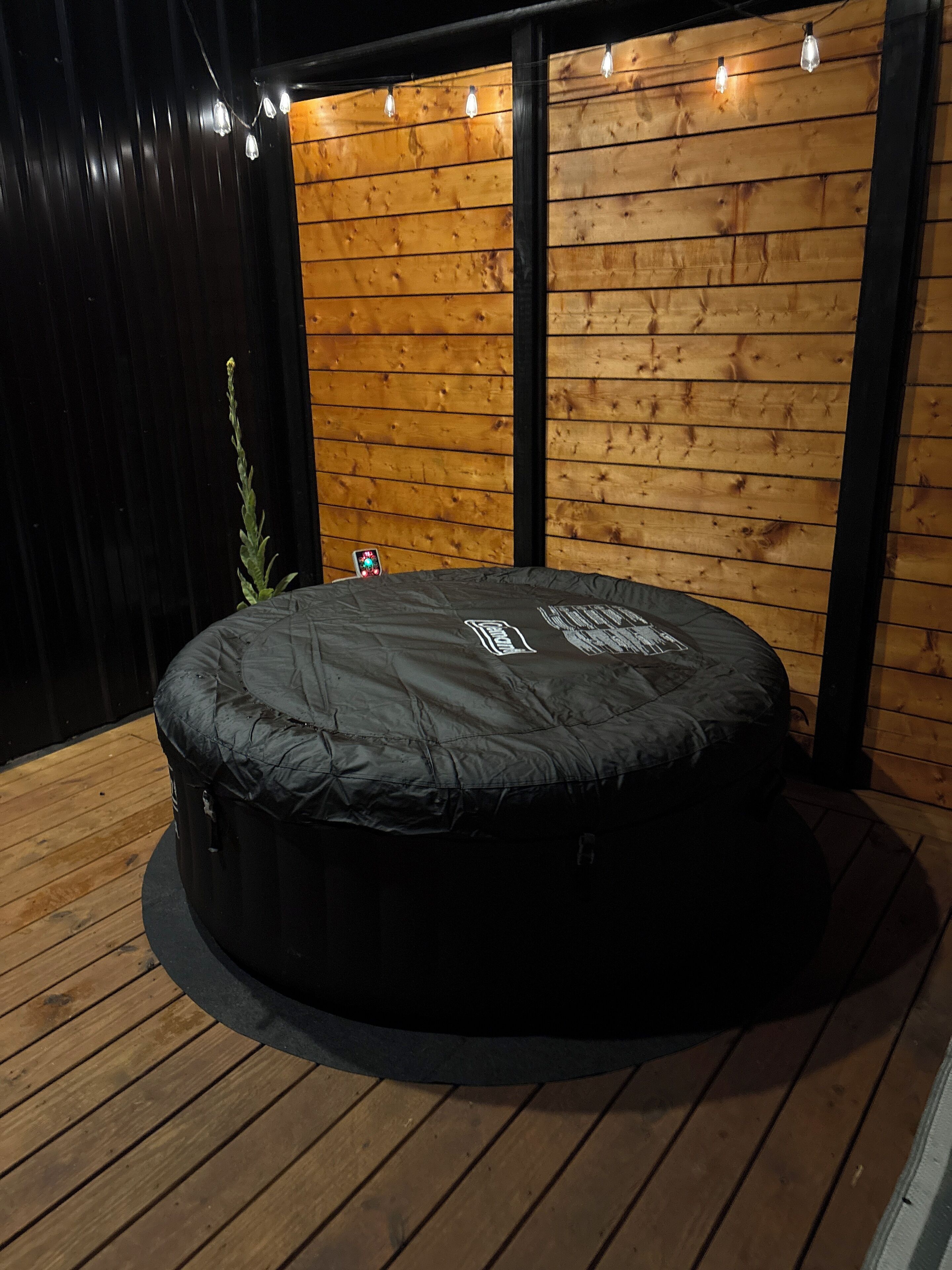 A round, black outdoor seating area with a wooden deck and a wooden wall with horizontal planks.