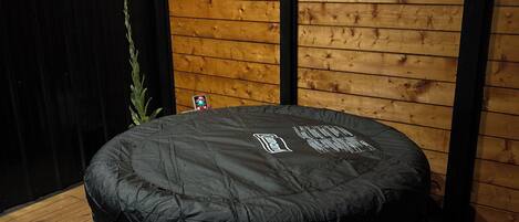 A round, black outdoor seating area with a wooden deck and a wooden wall with horizontal planks.