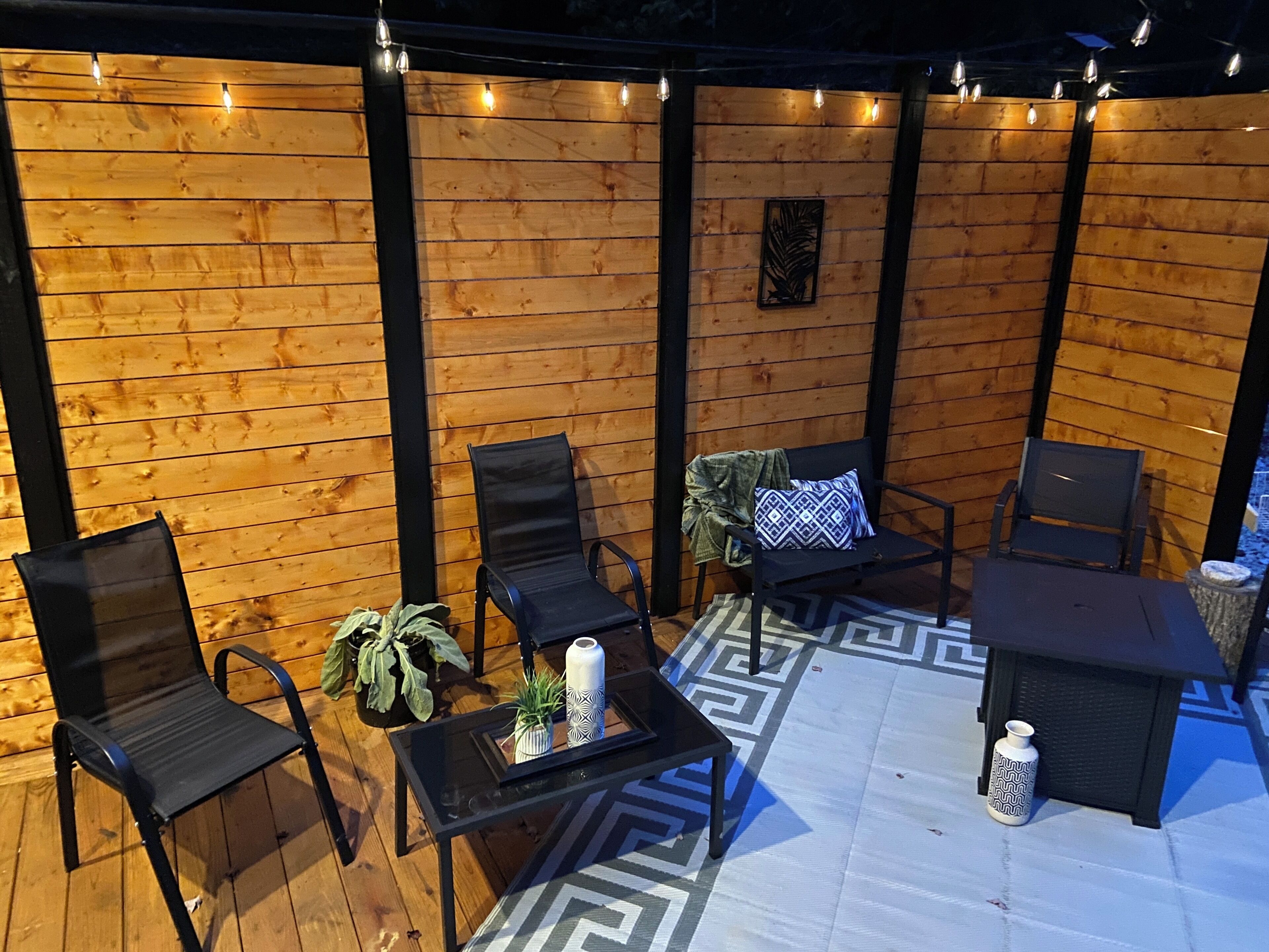 Une terrasse en bois, aménagée avec du mobilier d’extérieur, notamment des chaises et une table, ainsi qu’un tapis à motifs.