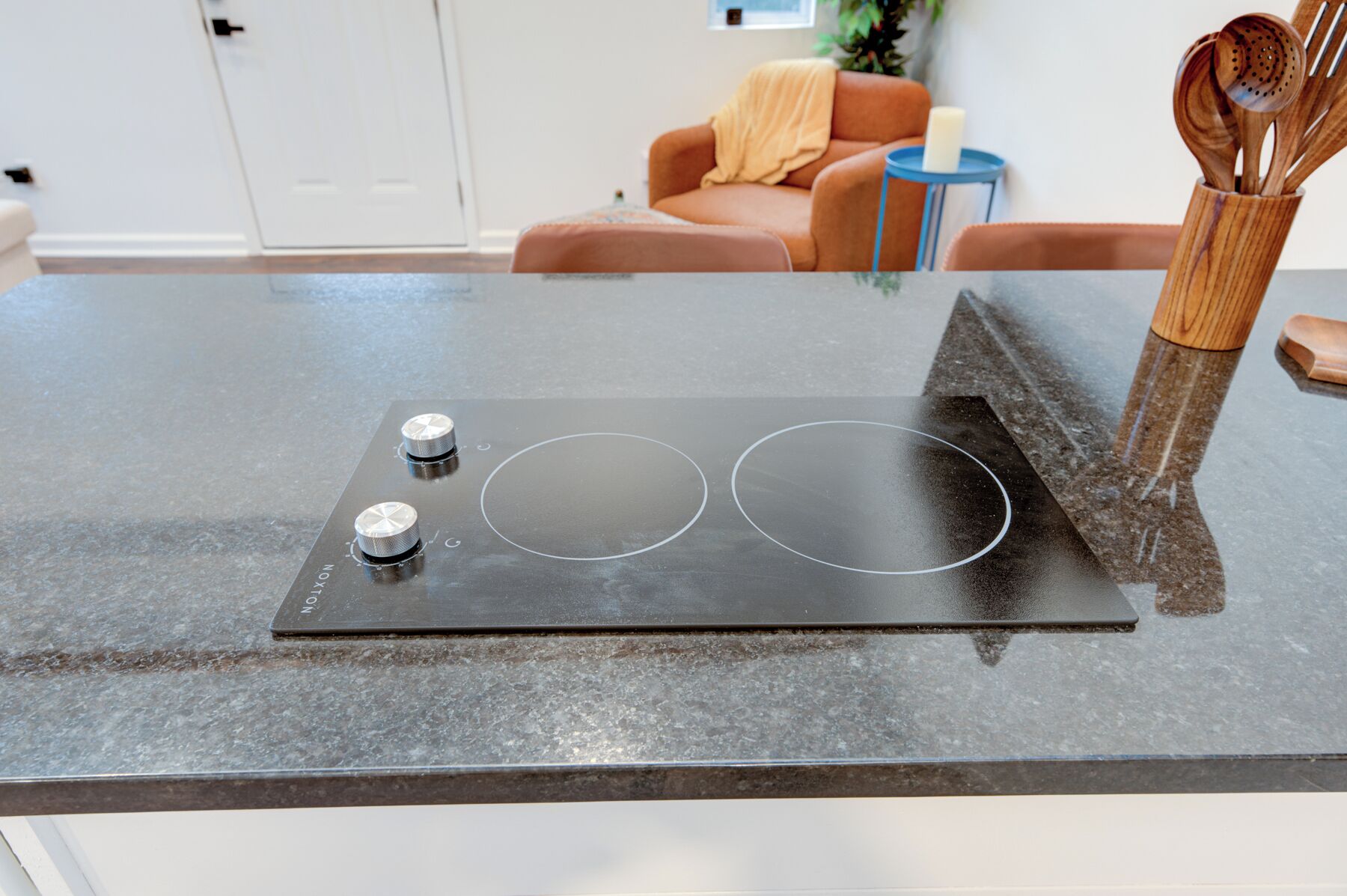 A kitchen with a black induction cooktop, two knobs, and a wooden utensil holder.