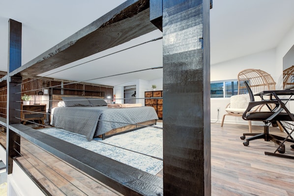 A modern bedroom with a bed, wooden flooring, and a desk with a chair.