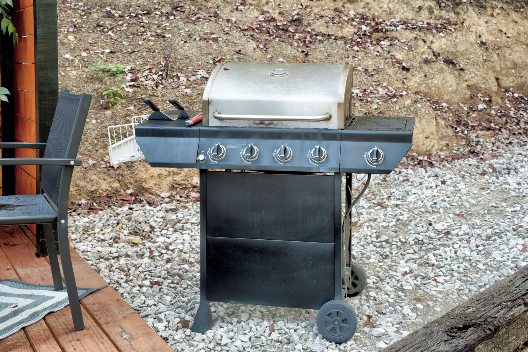 A portable grill with four burners and a lid, placed on a gravel surface.