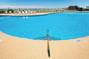 A clear blue pool with a metal ladder, lounge chairs, and a fence in the background.