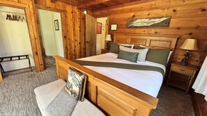 Un dormitorio con estructura de madera, una cama, mesitas de noche y un banco.