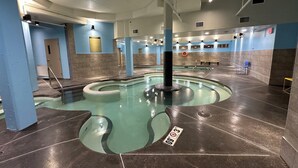 An indoor swimming pool with a circular design, surrounded by walls with blue and beige tiles, and a ceiling with visible lighting fixtures. - Solara Corner Suite-Pool & Hot Tub & Spa (Canmore)
