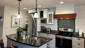 A modern kitchen with granite countertops, stainless steel appliances, and pendant lighting. - Solara Corner Suite-Pool & Hot Tub & Spa (Canmore)