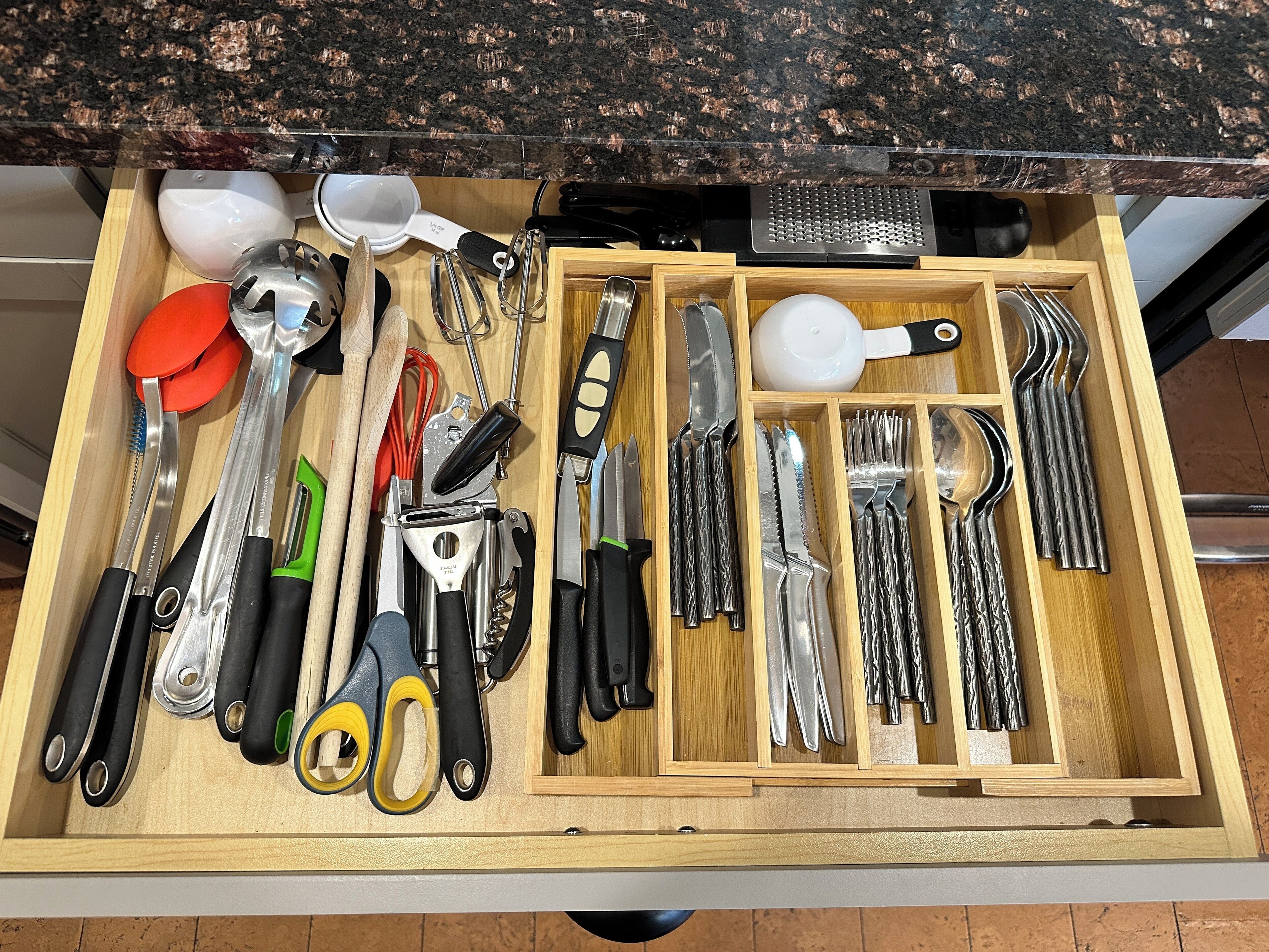 Un cajón con distintos utensilios y herramientas de cocina, incluyendo cuchillos, tijeras y un rallador.