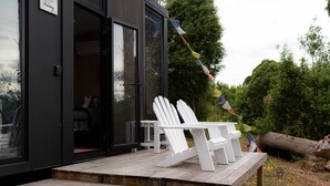 A modern house with a wooden deck, two white Adirondack chairs, and a flag.