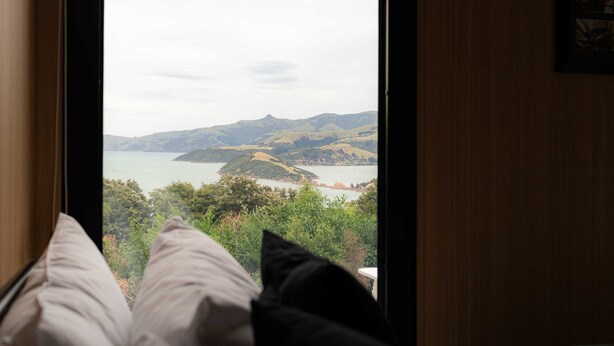A view from a window with a wooden frame, looking out to a landscape with hills and a body of water.