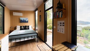 A bedroom with a bed, a desk, a bookshelf, and a view of the outdoors.