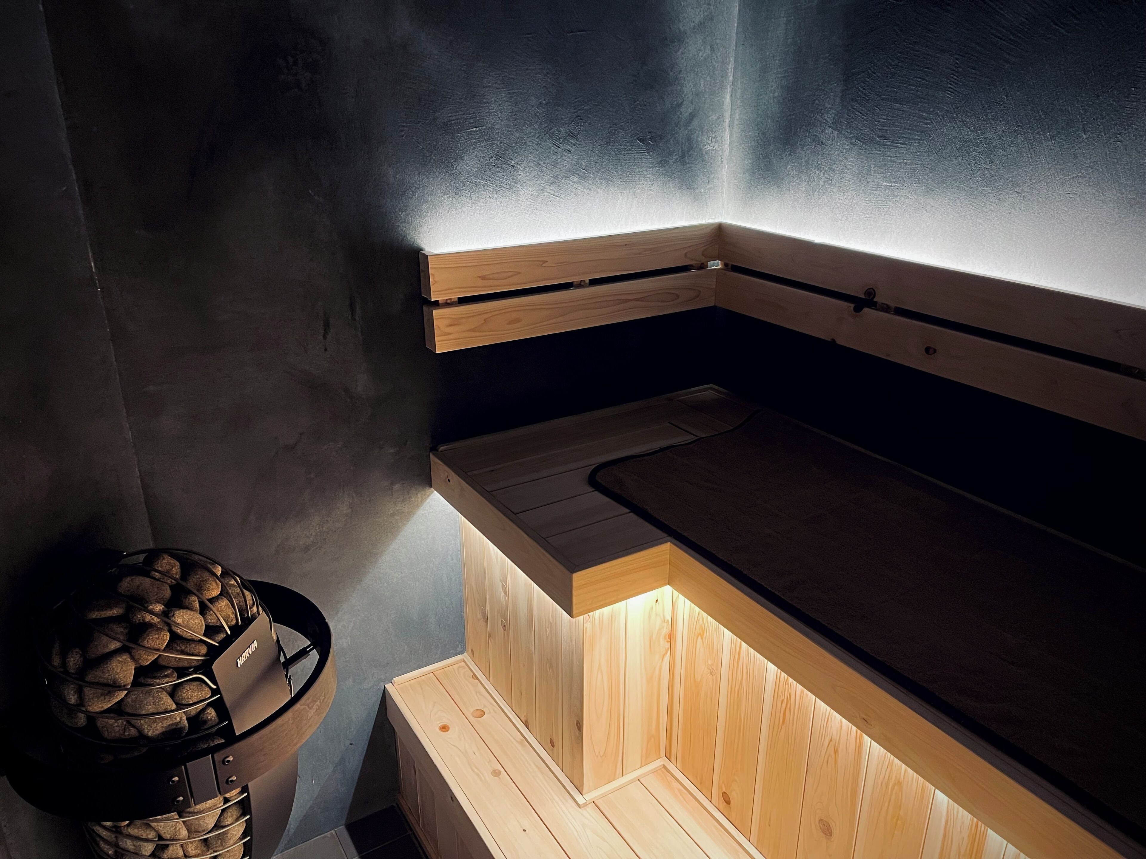 Een sauna met een houten bank, een handdoekrek en een mand vol aanmaakhout.