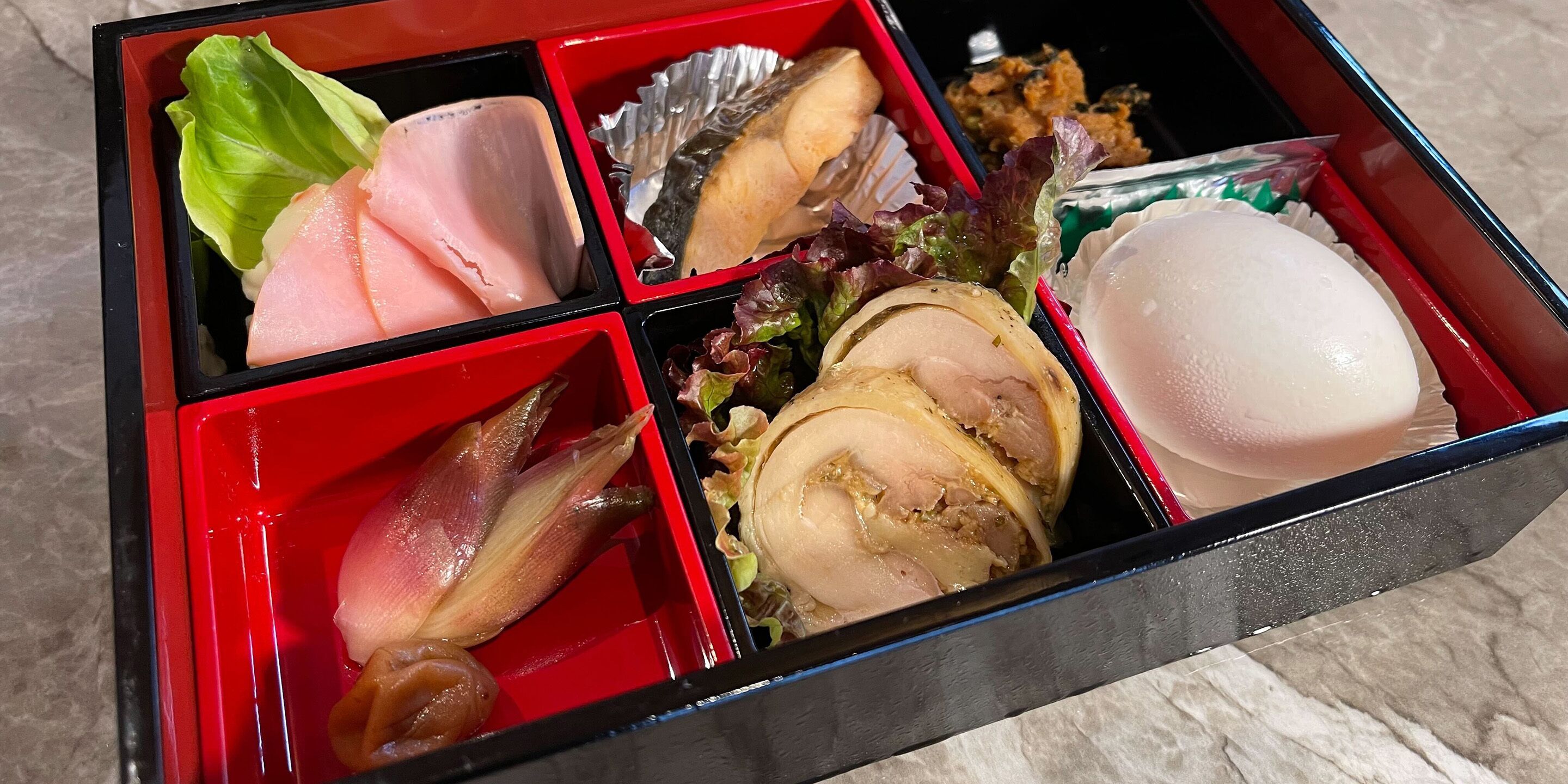 Una caja bento con diversos alimentos, incluyendo pescado, verduras y un huevo duro.