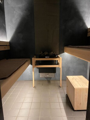 Una stanza compatta con un letto a castello, un piccolo tavolo di legno e una stufa a legna Harvia.
