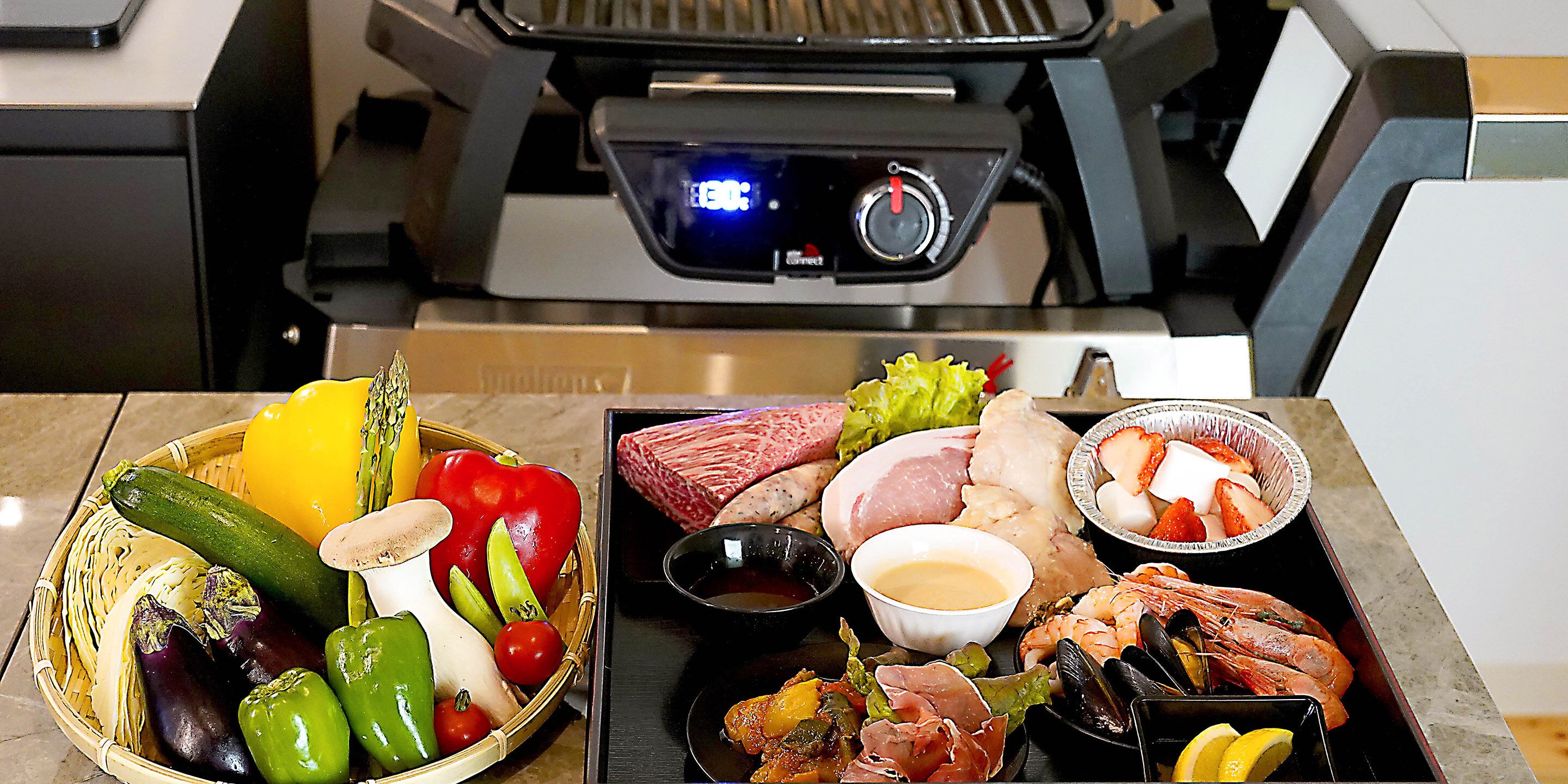 A variety of seafood and vegetables on a table with a grill in the background.