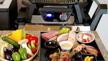 A variety of seafood and vegetables on a table with a grill in the background.