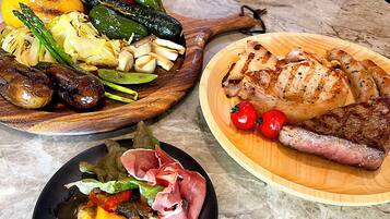 A variety of dishes including grilled meats, vegetables, and sausages on wooden serving platters.