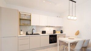 Una cocina moderna con armarios blancos, encimera de mármol, horno integrado y zona de comedor con mesa y sillas blancas.