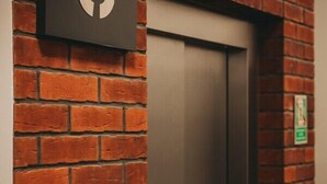 Un muro de ladrillo con una puerta y un cartel con un símbolo blanco.