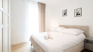 Una cama bien hecha con sábanas blancas, una mesita de noche y dos cuadros en la pared.