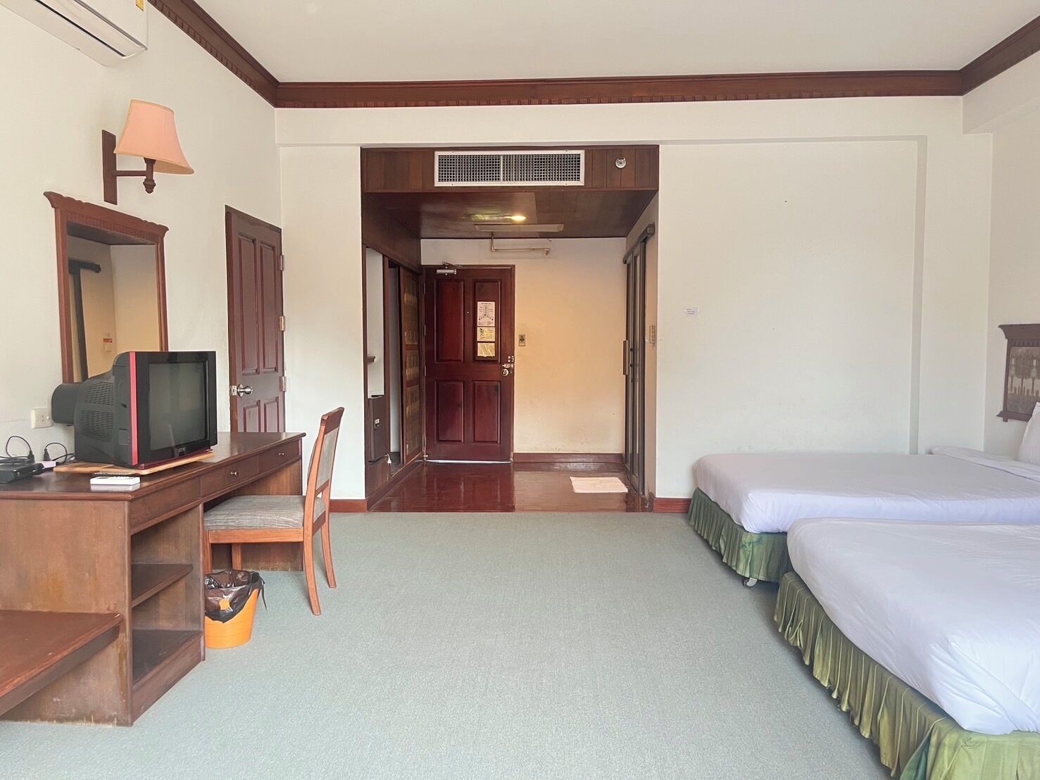 A hotel room with a desk, chair, TV, bed, and a door leading to another room.