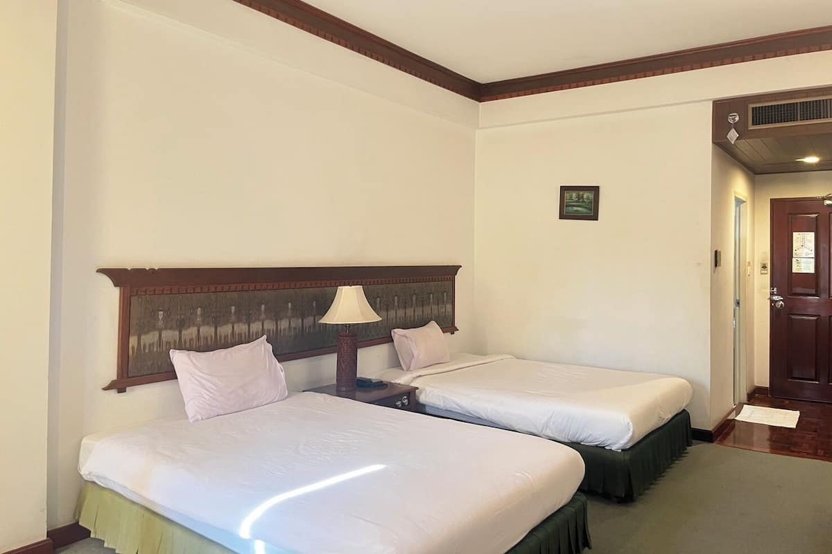 A hotel room with two single beds, a wooden headboard, a nightstand with a lamp, and a small painting on the wall.