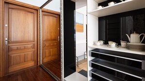 Una habitación con puertas de madera, un estante blanco con utensilios de cocina y un armario negro.