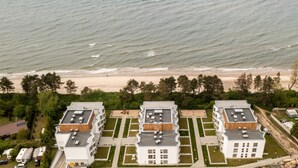 A coastal hotel with three white buildings, a sandy beach, and a forested area. - 2Homerent Piedra | Relax with a Baltic Sea View (Gąski)