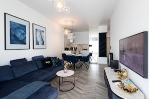 A modern living room with a sofa, dining area, kitchen, and a large TV. - 2Homerent Piedra | Relax with a Baltic Sea View (Gąski)