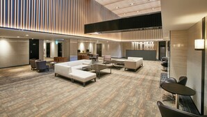 Un hall espacioso con diseño moderno, que incluye una amplia zona de estar con sofás y sillones, una mesa de centro y un techo alto con listones verticales de madera.