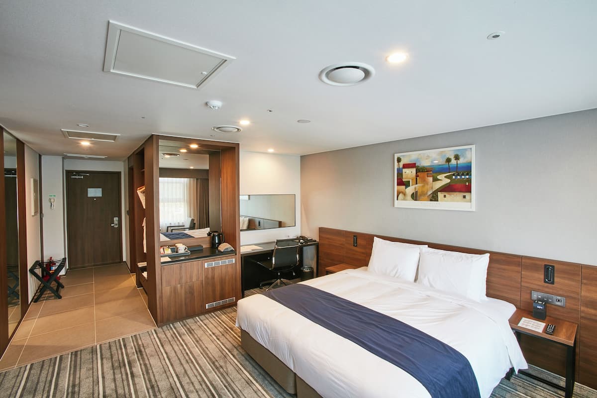 A hotel room with a bed, desk, and a large mirror.