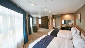 Habitación de hotel con dos camas, un ventanal con cortinas, un espejo y un área de descanso.