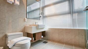 A modern bathroom with a toilet, sink, mirror, and window with blinds.